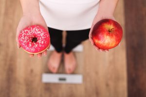 Woman on a scale holding a donut and an apple