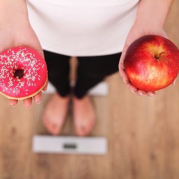 Woman on a scale holding a donut and an apple
