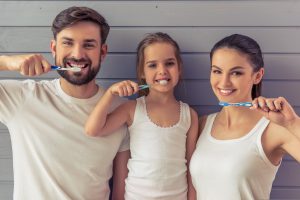 young parents and their cute little daughter are looking at camera and smiling while brushing teeth focusing on preventative dentistry in Greensburg, PA